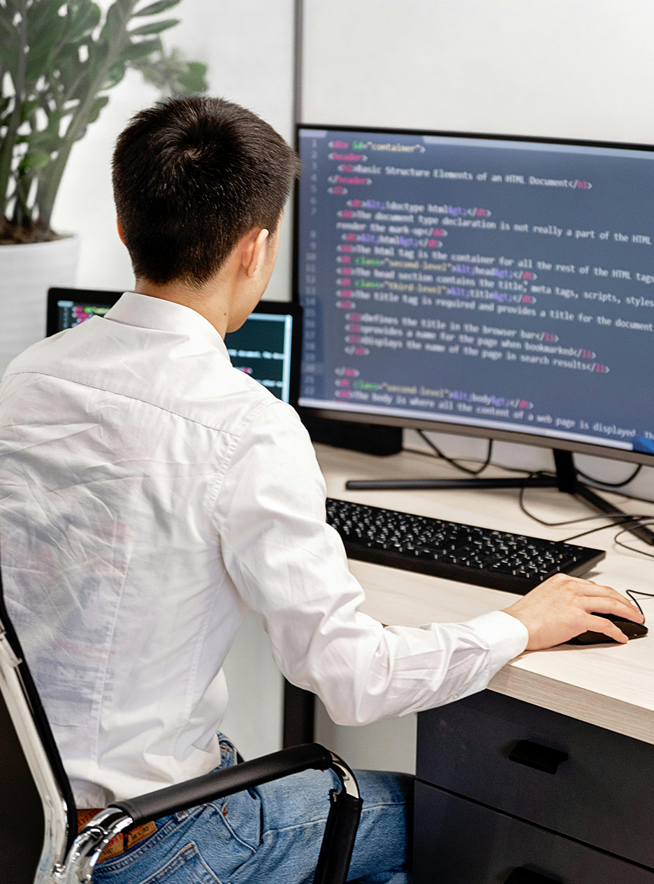 Male software developer writing code on a multi-screen workstation, representing custom software development and enterprise application engineering.